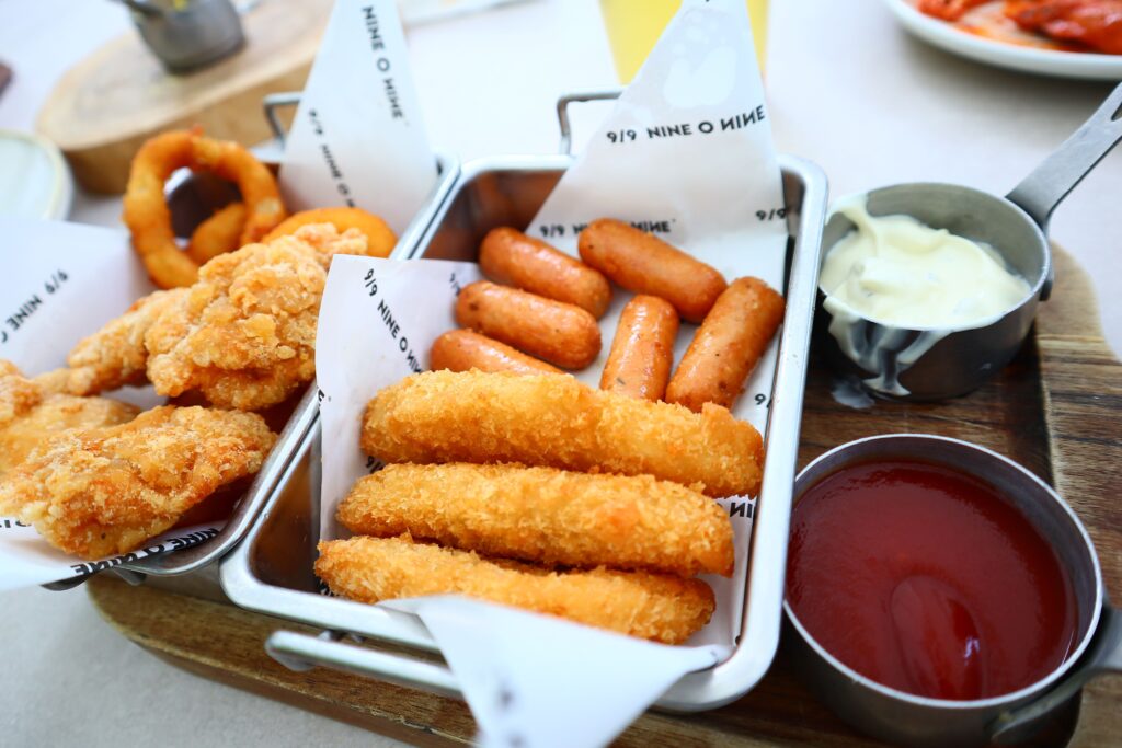 Variety of fried snacks including onion rings, sausages, and nuggets with ketchup and mayo.